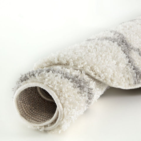 A plush rolled-up moroccan ivory shaggy rug in soft white and gray with subtle striped patterns