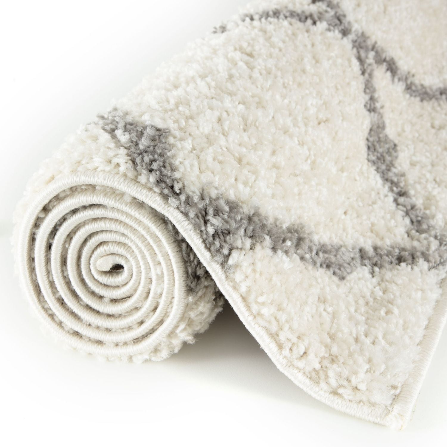 A plush moroccan ivory shaggy rug with soft gray geometric patterns rolled neatly on a white surface