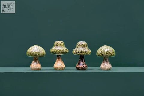 Four moss mushroom figurines with textured green caps and speckled brown stems in light stone ceramic material