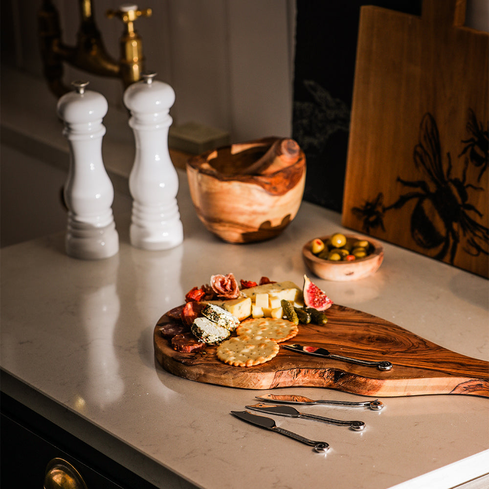 A rustic olive wood cutting board with natural edges and grain paired with mouse mini cheese knives set of 4