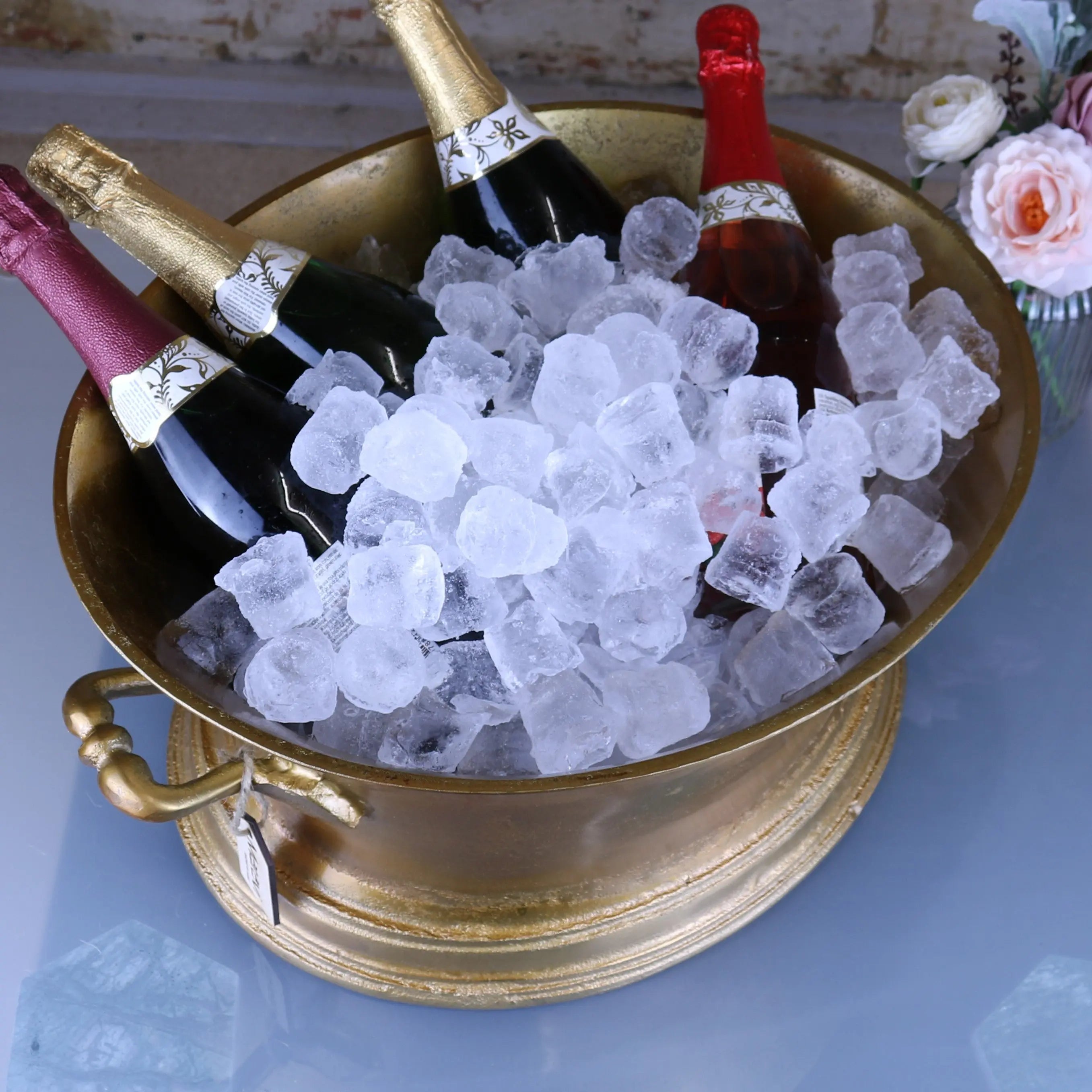 Gold metal moyar champagne bucket with ornate handles and base filled with clear ice cubes for ice bath use