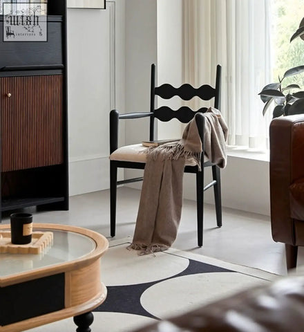Black wooden mucha dining chair with wavy backrest and beige cushioned seat draped with taupe fringed throw blanket