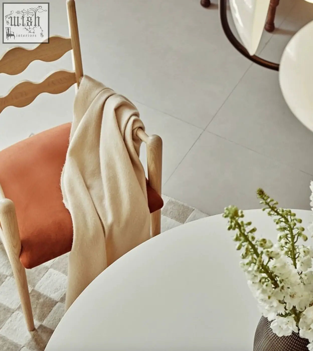 A cream woolen sweater hanging over a mucha dining chair with a wooden frame and orange upholstered seat