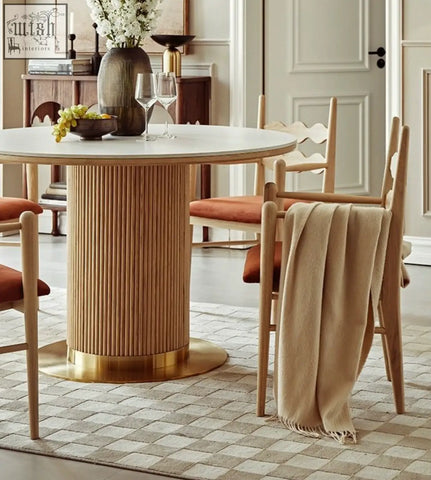 A modern round dining table with a white marble top and fluted wooden base paired with mucha dining chair