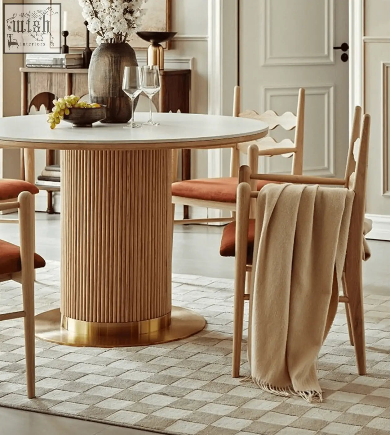 A round dining table with a light wood ribbed pedestal base and brass foot paired with mucha dining chair