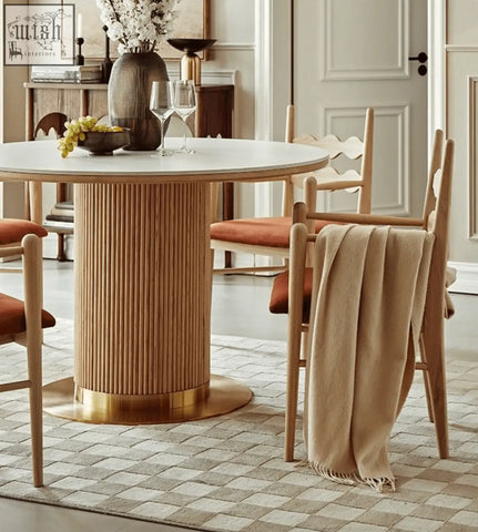 A round dining table with a light wood ribbed pedestal base and brass foot paired with mucha dining chair