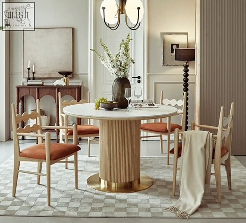 Round dining table with white marble top and vertical wood grain pedestal base with gold foot, perfect for mucha dining chair setups