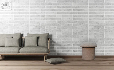 Gray upholstered sofa with wooden legs and matching throw pillows against white brick wall featuring mud boucle fabric