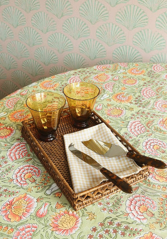 Woven rattan serving tray with beige white checkered napkin and amber tumblers on mughal rajan floral tablecloth