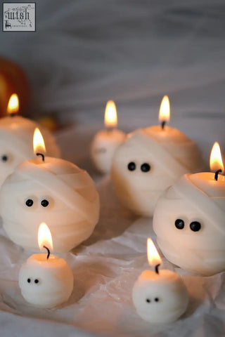 White mummy ghost candles with black bead eyes and lit wicks perfect for spooky halloween decor