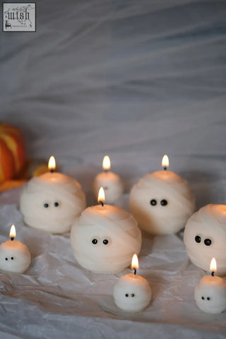 White mummy ghost candles with black bead eyes and lit wicks perfect spooky decor ghost candles