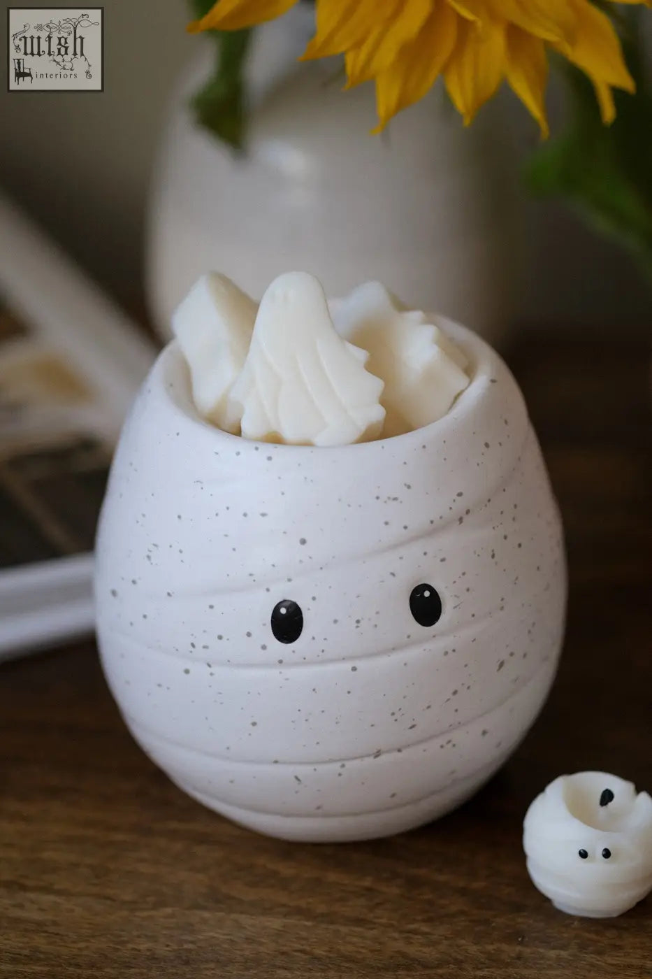 White speckled ceramic mummy shaped wax melt burner with black eyes holding white wax melts for fragrance oil use