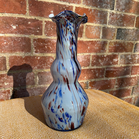 A murano tall glass vase with a fluted rim and blue red white swirling patterns on translucent glass