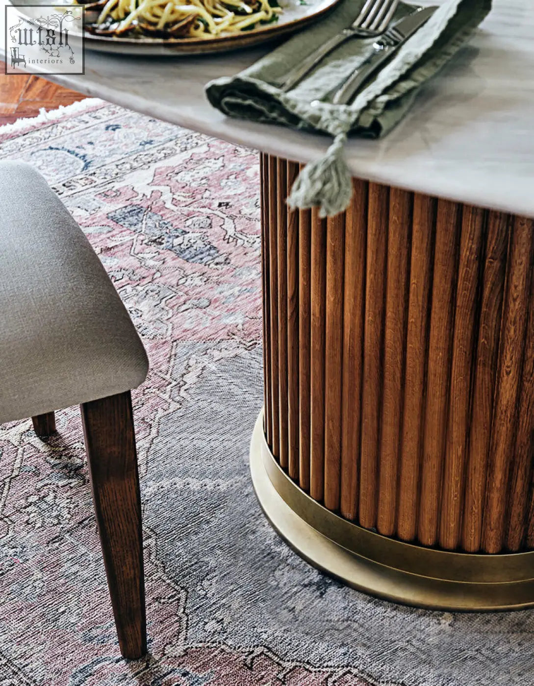 A sleek murcell oval dining table with polished marble top and fluted wooden base with brass ring accents