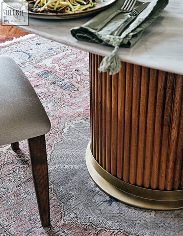 A sleek murcell oval dining table with polished marble top and fluted wooden base with brass ring accents