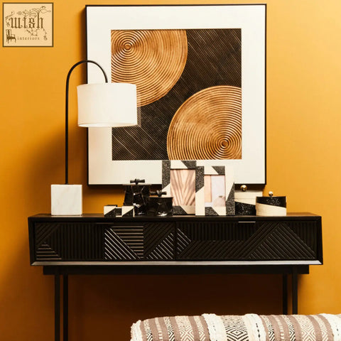Black console table with geometric ribbed front panels and slender legs beside murdoch curved table lamp with marble base and white fabric shade