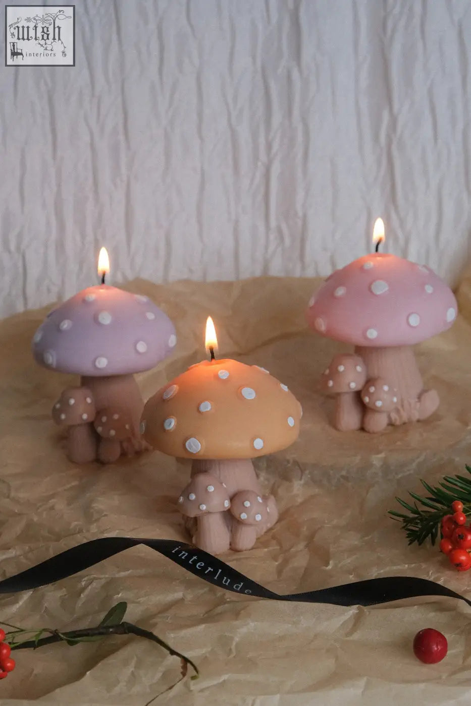 Three lit mushroom family candles with pastel purple peach pink polka dot caps and beige stems with smaller mushrooms