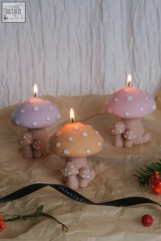 Three lit mushroom family candles with pastel purple peach pink polka dot caps and beige stems with smaller mushrooms
