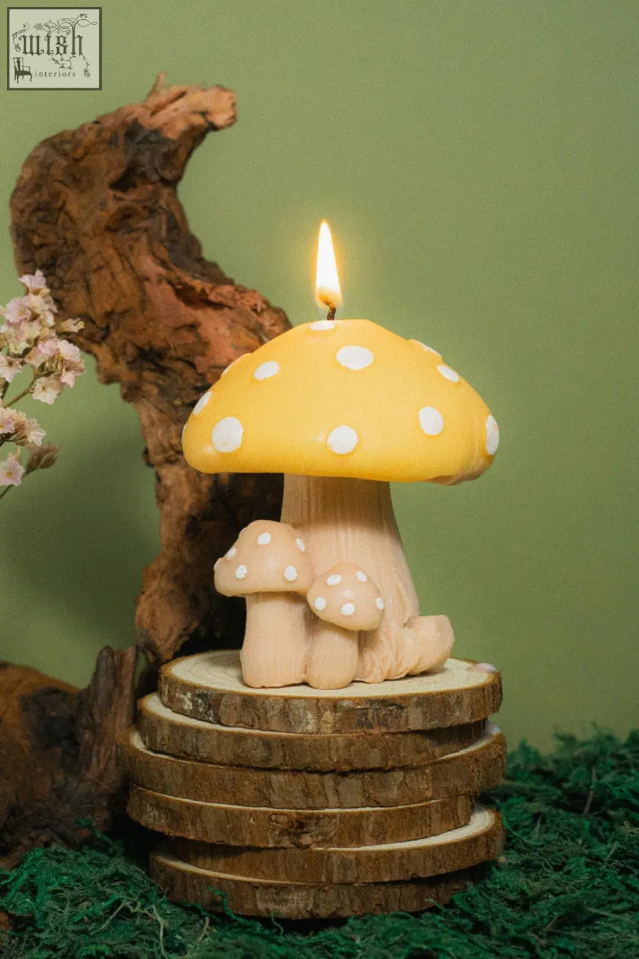 A yellow mushroom family candle with white polka dots and a lit wick featuring two smaller matching candles at the base