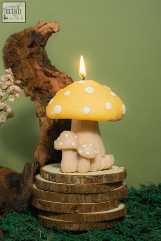 A yellow mushroom family candle with white polka dots and a lit wick featuring two smaller matching candles at the base