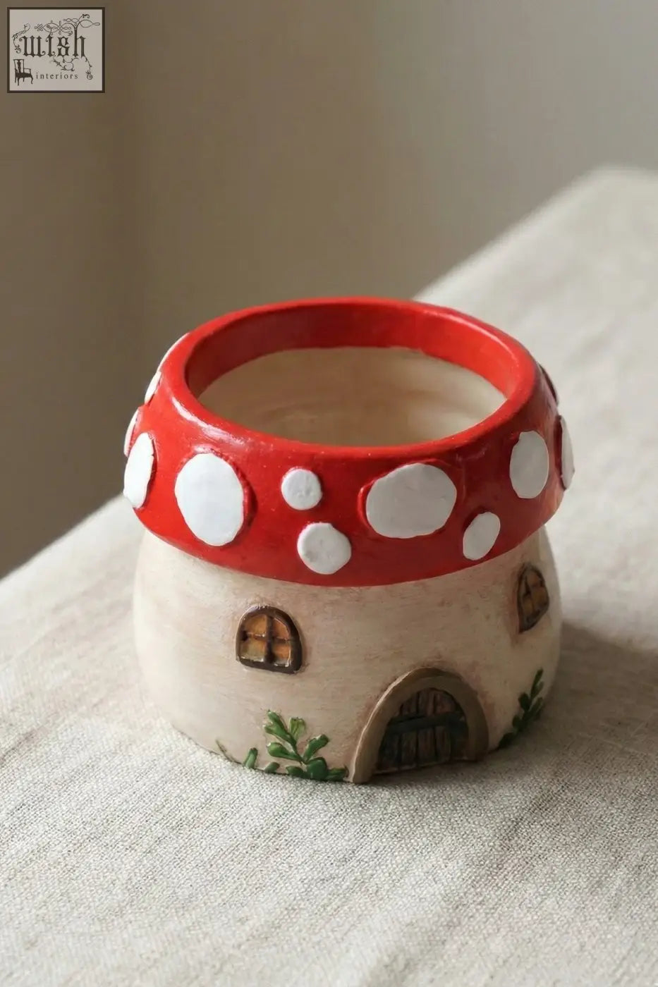 A charming red and white ceramic mushroom tealight holder with painted windows door and greenery accents