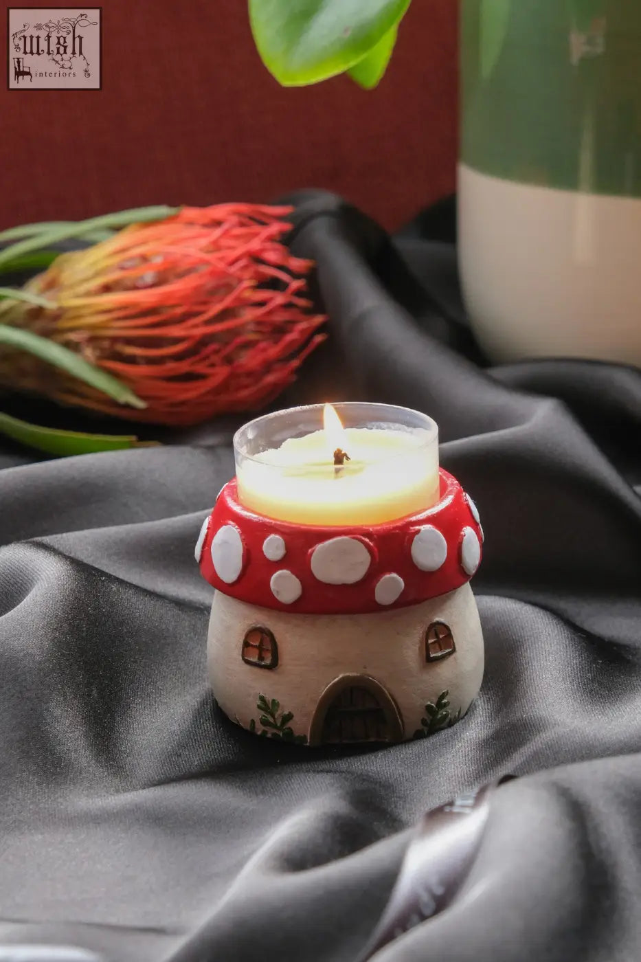 A red and white ceramic mushroom tealight holder with a lit yellow wax candle inside for cozy lighting