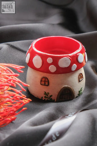 A charming red and white ceramic mushroom tealight holder with painted windows door and greenery accents