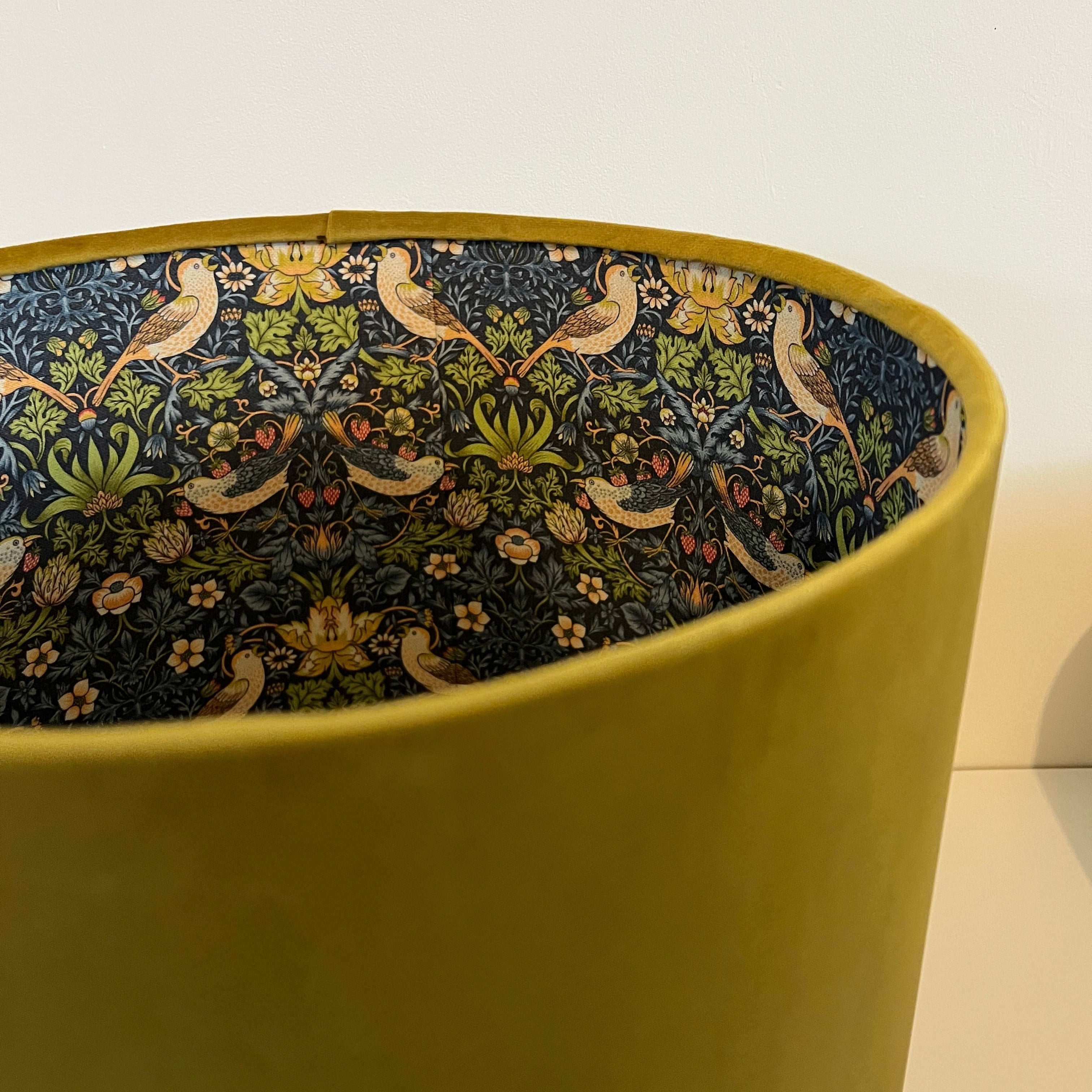 A mustard velvet double sided drum lampshade with a navy bird and floral interior pattern for ceiling light shade