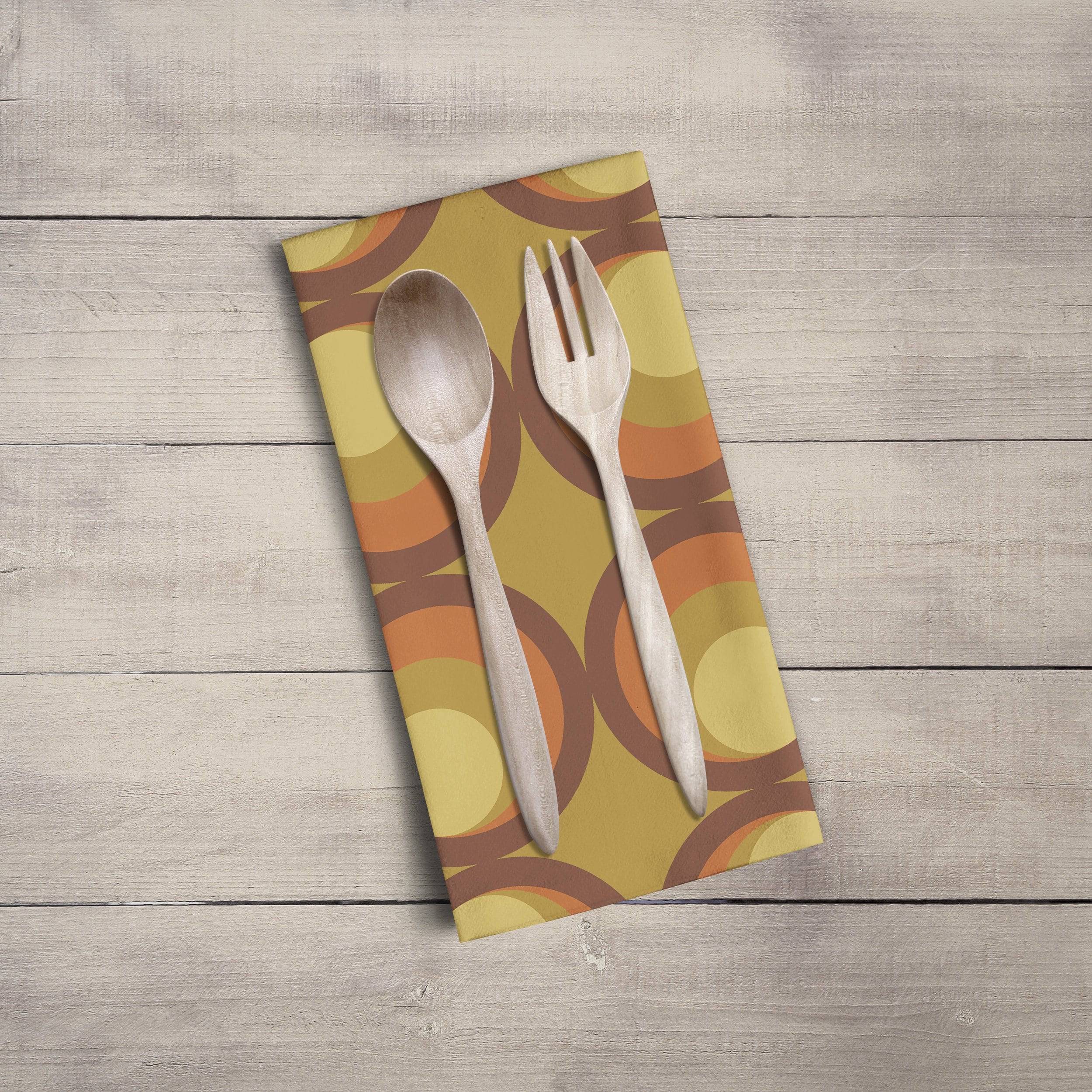 A mustard yellow tea towel with a retro orange and brown circular pattern featuring wooden spoon and fork