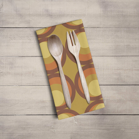 A mustard yellow tea towel with orange and brown retro circular pattern featuring wooden spoon and fork