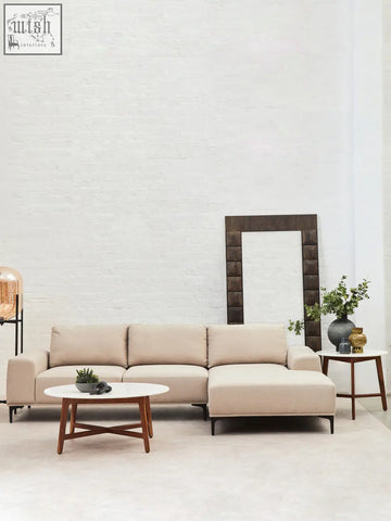 Beige leather sectional sofa with chaise lounge and wooden legs next to myan acacia wood and white marble round side table