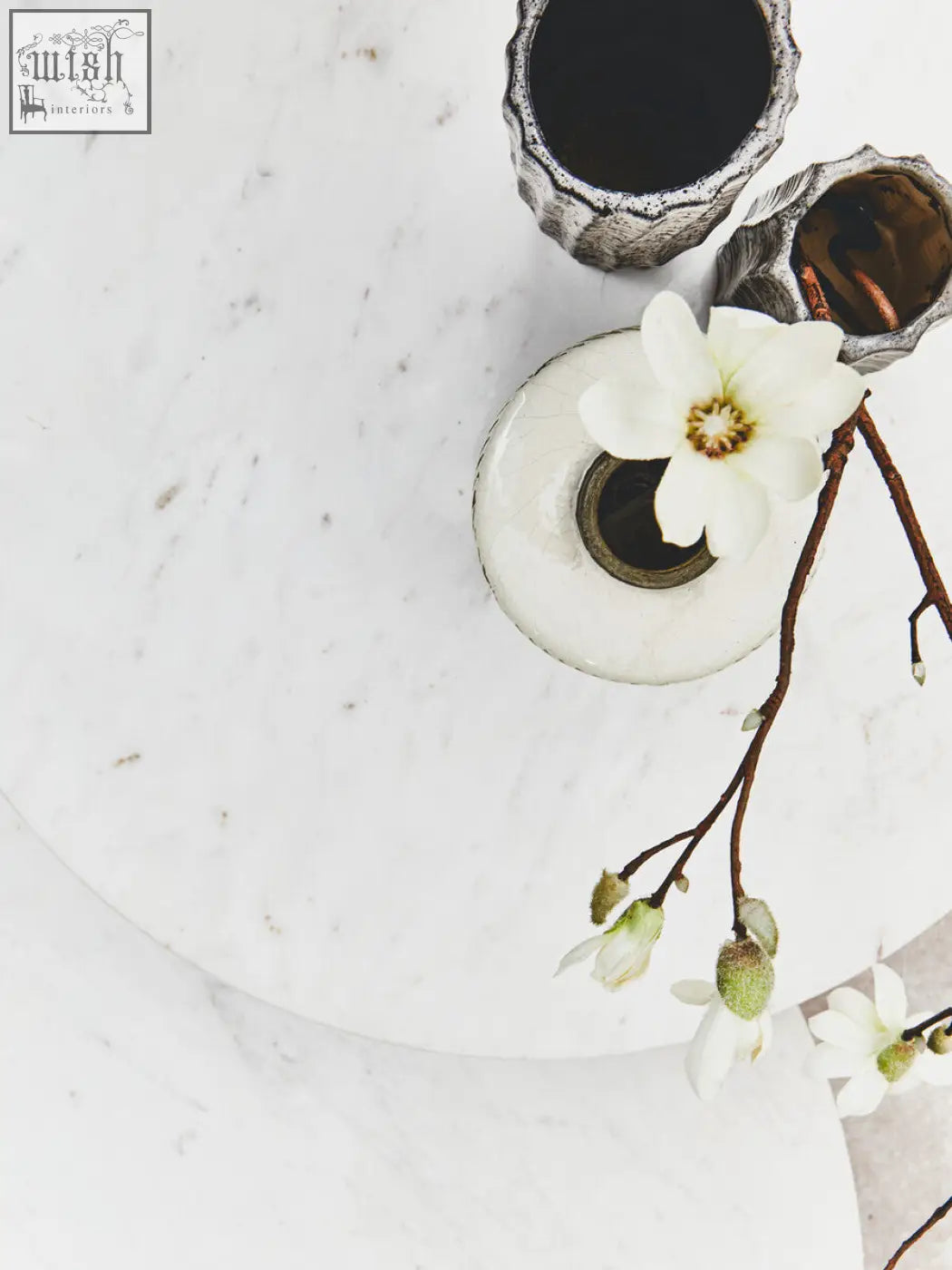 A delicate white magnolia flower in a round vase on a white marble round side table with acacia wood legs