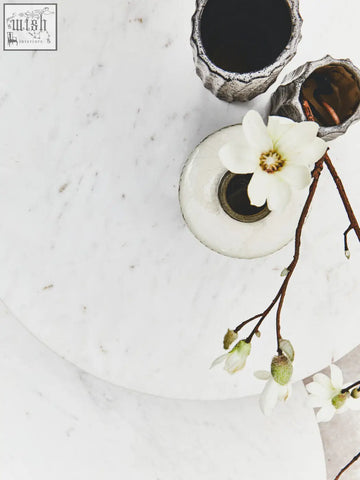 A delicate white magnolia flower in a round vase on a white marble round side table with acacia wood legs