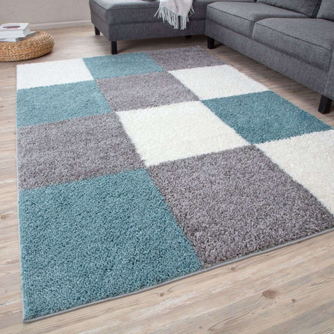 A plush shaggy area rug with a geometric patchwork design in duck egg blue gray and cream colors