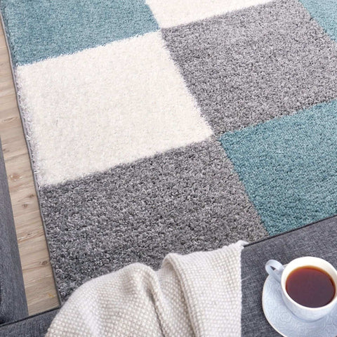 A plush shaggy area rug with a geometric patchwork design in duck egg blue gray and cream shades
