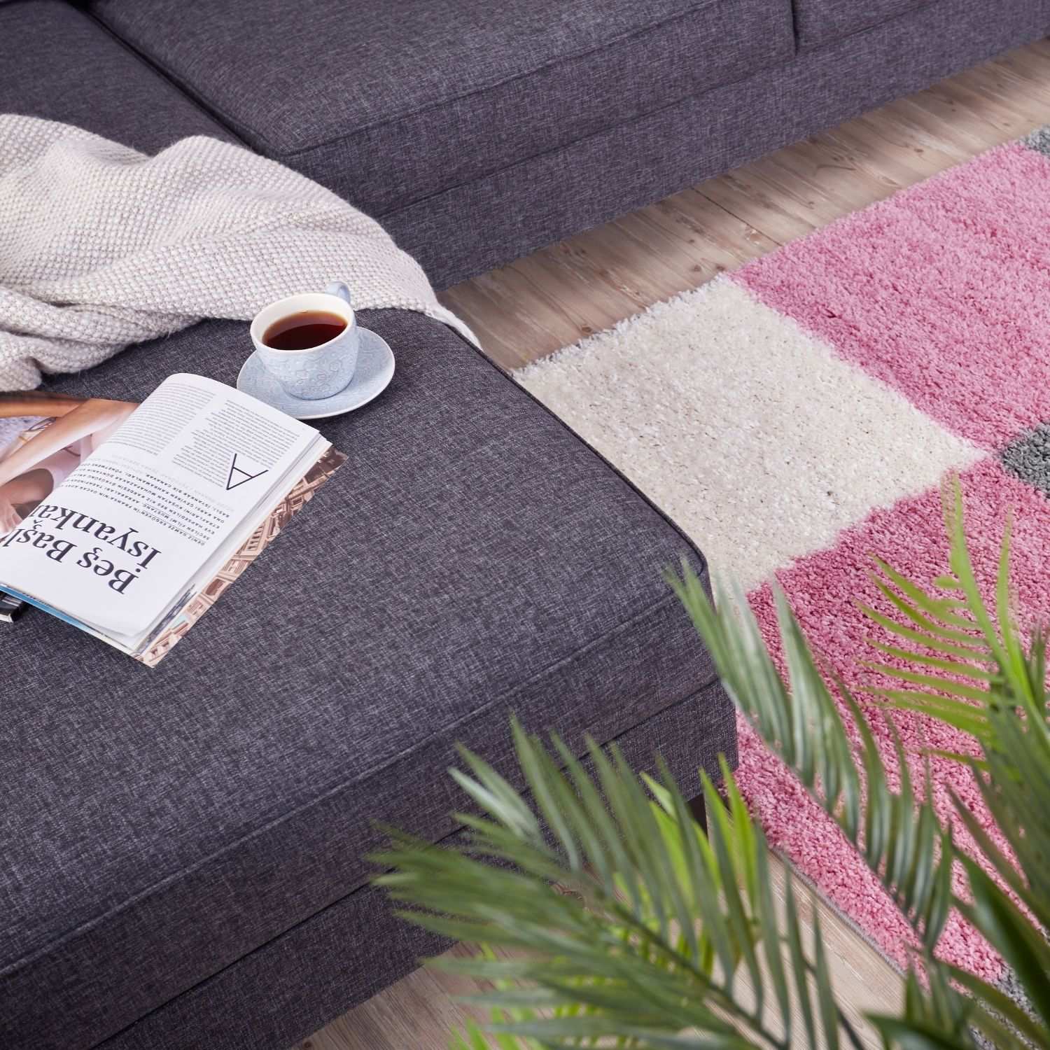 A cozy gray textured sofa with a cream throw on a soft myshaggy geometric pink rug in the living room