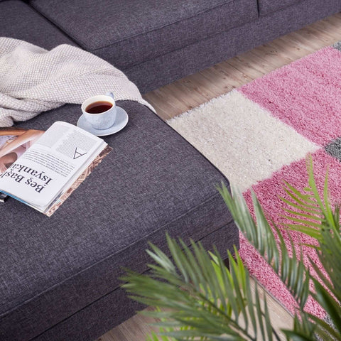 A cozy gray textured sofa with a cream throw on a soft myshaggy geometric pink rug in the living room