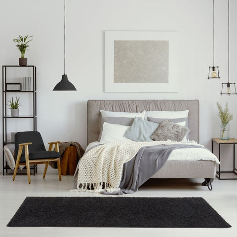 Gray upholstered bed with tufted headboard and layered bedding on cozy myshaggy solid black rug