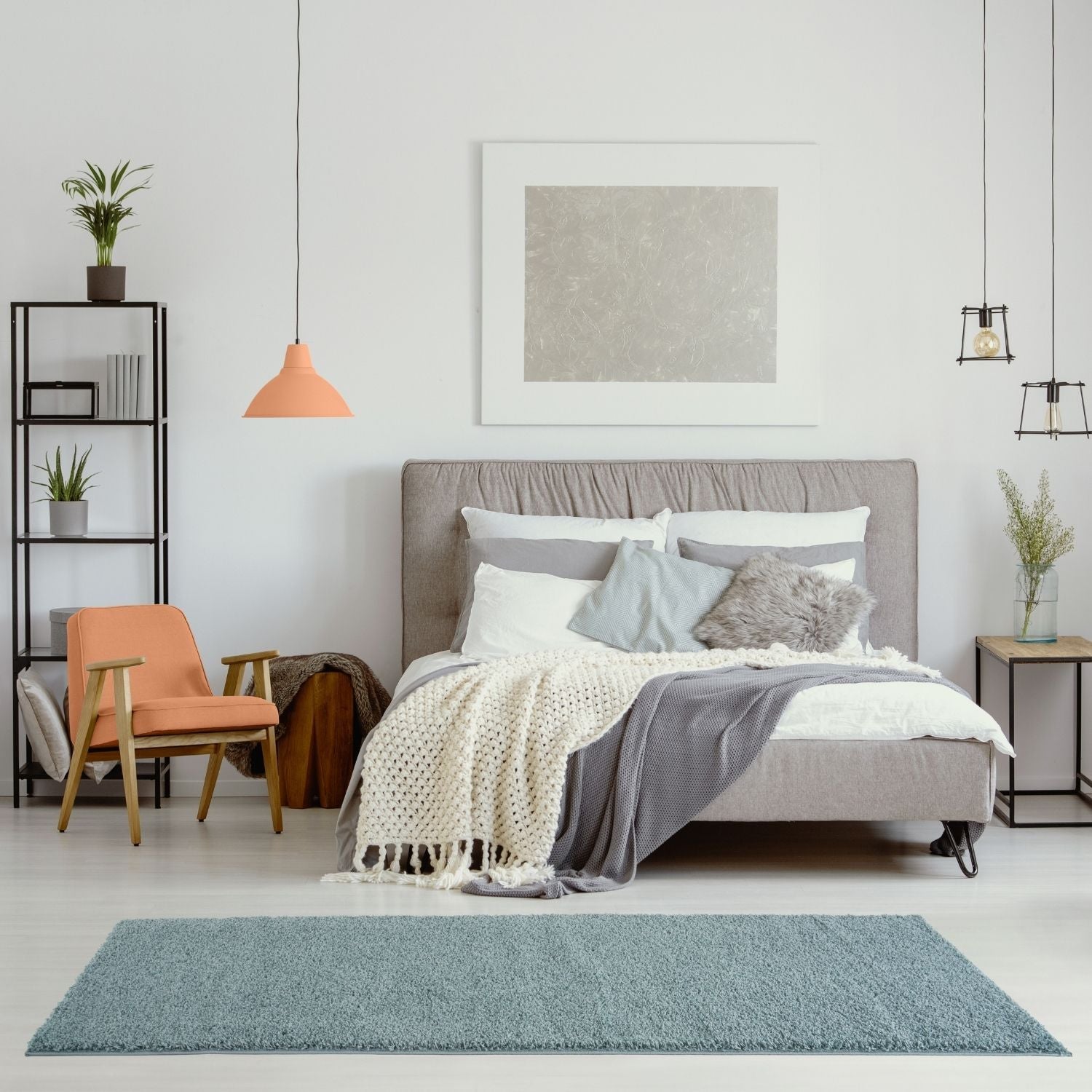 Gray upholstered bed with multiple pillows and layered blankets on a duck egg blue rug for cozy bedroom style