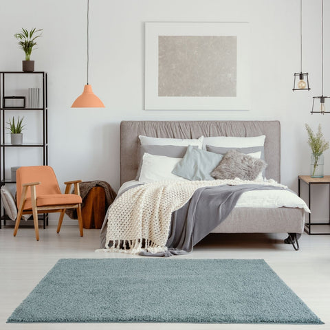 Gray upholstered bed with tufted headboard and layered bedding beside a duck egg blue solid Myshaggy rug