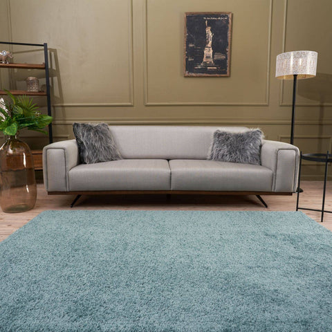 Light gray upholstered sofa with wooden legs and faux fur pillows on a duck egg blue rug