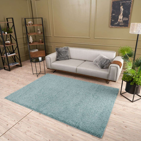 A plush light teal rectangular shaggy rug in duck egg blue lays centered on a wooden floor perfect for cozy spaces