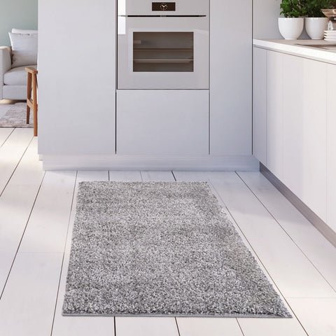 A plush myshaggy solid grey rug with a soft textured surface on a white wooden floor perfect for cozy spaces