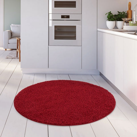 A plush circular myshaggy solid red rug with soft shaggy texture on a white wooden floor