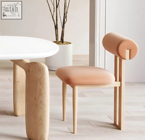 A blush pink upholstered chair with a minimalist wooden frame and cylindrical backrest for namie dining table