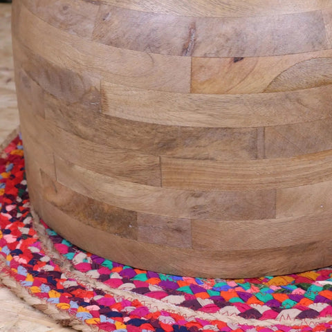 A light brown cylindrical wooden ottoman made of horizontally stacked narmada swirl mango wood slats