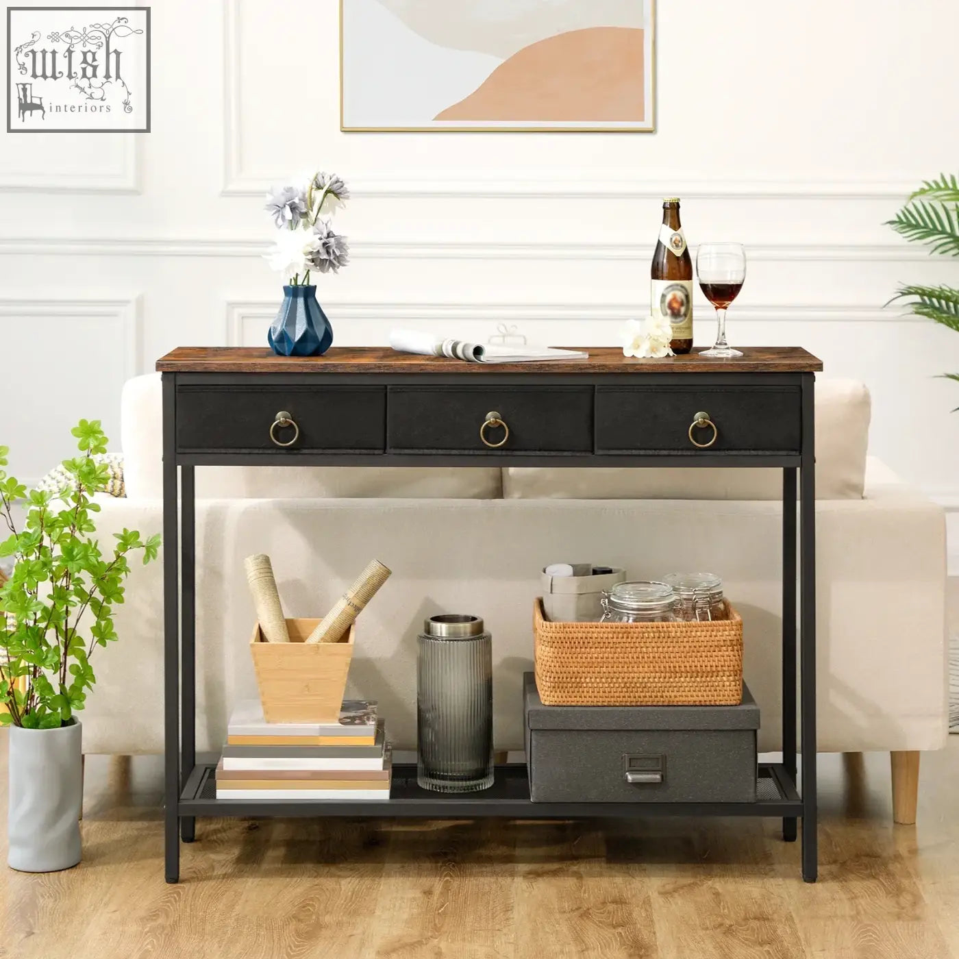 Narrow entryway console table with black metal legs, dark wood top, three drawers with round brass handles and antique appearance