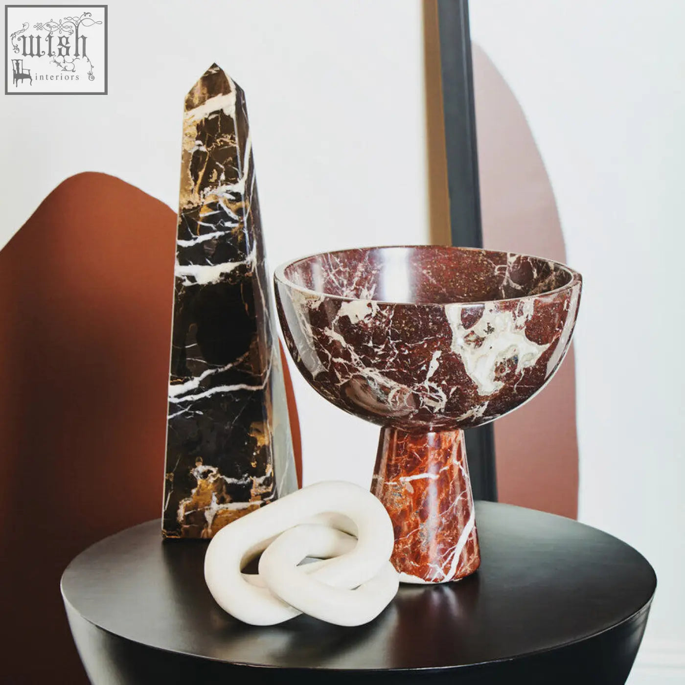 A reddish-brown marble bowl with a flared rim and slender base next to a white marble three link chain sculpture
