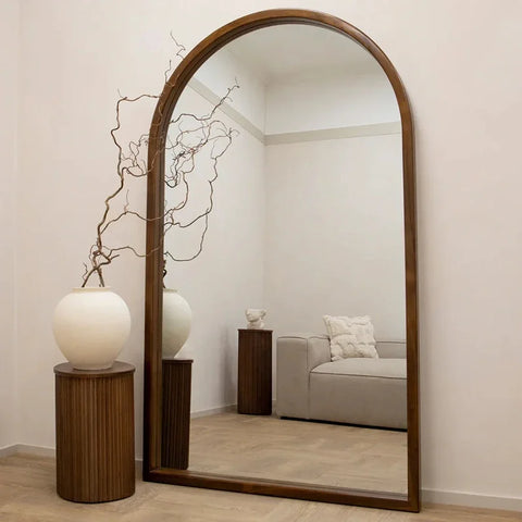A tall natsuki mirror with a sleek dark wood frame reflecting a minimalist living room scene