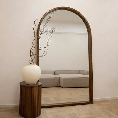 The natsuki mirror is a tall arched mirror with a dark wood frame reflecting a minimalist room decor